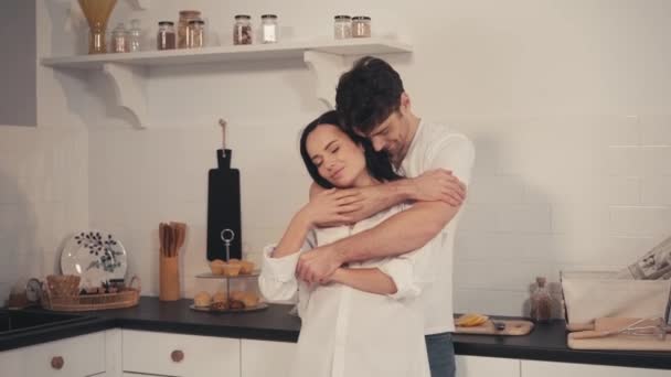 Genç adam modern mutfakta gözleri kapalı baştan çıkarıcı kız arkadaşını kucaklıyor. - Video, Çekim