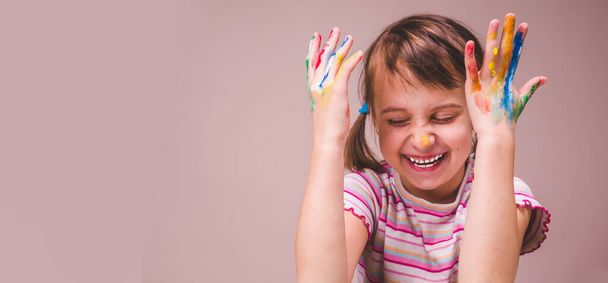 Kaunis nuori onnellinen tyttö lasten kasvot meikki ja maalaus värikkäitä käsiä. Vapaa tila tekstin tai suunnittelun. Valikoiva keskittyminen käsiin. Kopioi tilaa suunnittelu. - Valokuva, kuva