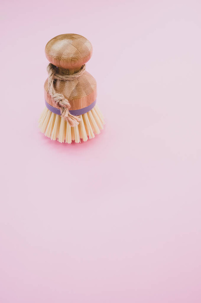 A closeup of a wooden round dishwashing brush on a pink surface - space for text - Фото, изображение