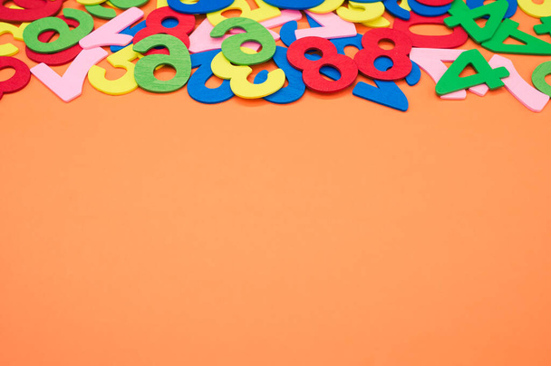 A closeup shot of the colorful wooden numbers scattered on an orange surface - space for text - Φωτογραφία, εικόνα