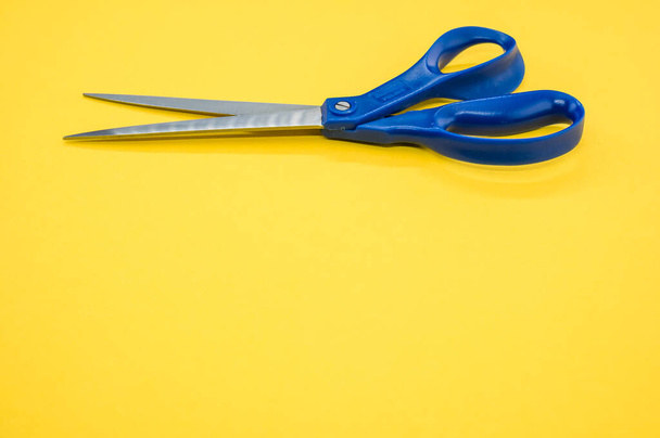 A closeup of metallic scissors on a yellow surface - space for text - Foto, Imagem