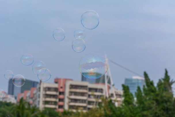 Una gran cantidad de burbujas de jabón volando en el parque con fondo de cielo azul y puesta de sol en los edificios - Foto, imagen