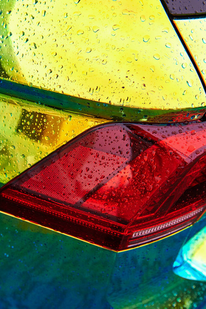 Chameleonské holografické barevné auto v dešti. Detailní záběr zezadu. Krásné moderní LED podsvícení detailní. Balení auta s duhovou barvou. Dešťové kapky na auto. Svislá fotografie. - Fotografie, Obrázek