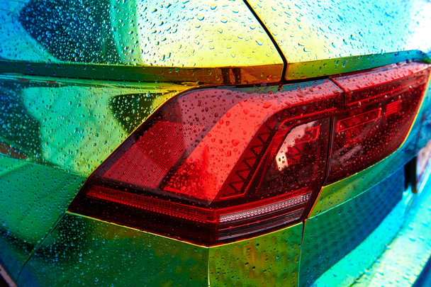 Kameleon holografische kleur auto in de regen. Achteraanzicht close-up. Mooie moderne LED achtergrondverlichting close-up. Autoverpakking met iriserende verf. Regendruppels op de auto. - Foto, afbeelding