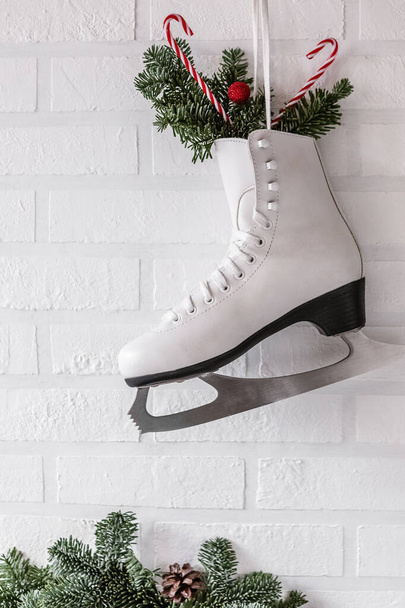 winter composition with figure skates and fir branches on the background of a white brick wall. - Фото, изображение