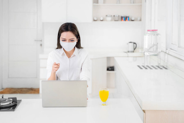 Young businesswoman wearing a mask while making video call on laptop and working from home during Covid-19 pandemic - Фото, зображення