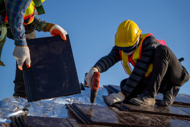 Fermer travailleur installer un nouveau toit de tuiles en céramique avec des outils de toiture Perceuse électrique utilisée dans le chantier de construction. - Photo, image