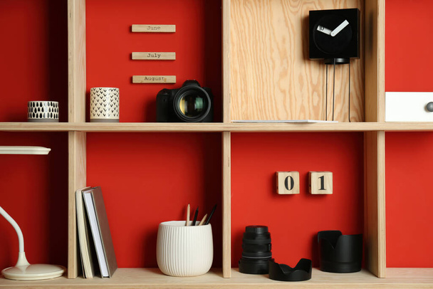 Stylish wooden shelves with photography equipment and decorative elements on red wall - Фото, изображение