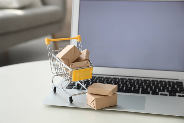 Internet shopping. Laptop and small cart with boxes on table indoors - 写真・画像