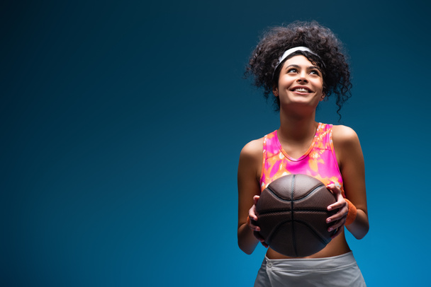 веселая женщина в спортивной одежде держит баскетбол на голубом - Фото, изображение
