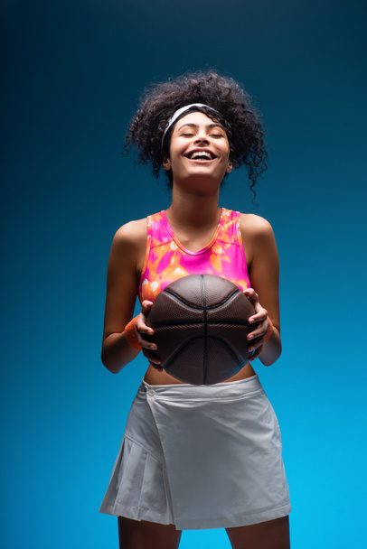 smiling woman in sportswear holding basketball on blue - Foto, imagen