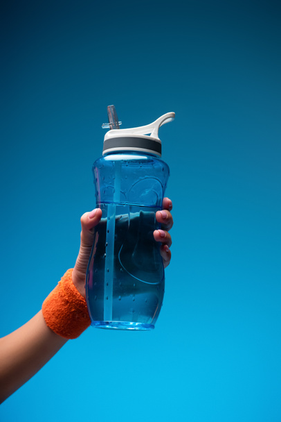 Ausgeschnittene Ansicht einer Frau mit Sportflasche auf blauem Grund - Foto, Bild