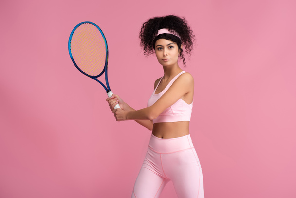 young curly sportswoman holding tennis racket while playing isolated on pink - Φωτογραφία, εικόνα