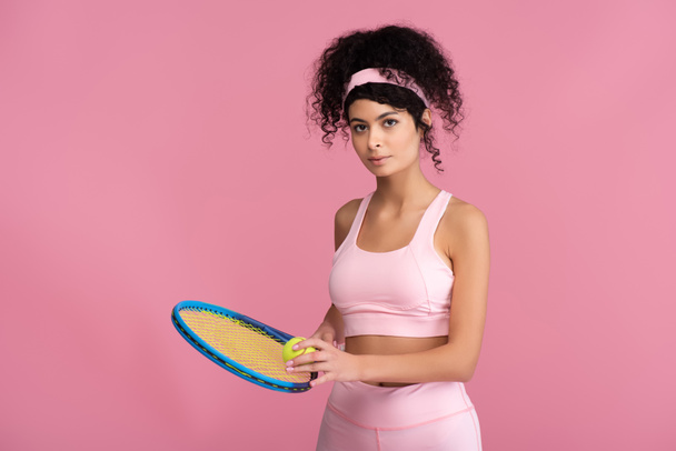 joven mujer deportiva sosteniendo raqueta de tenis con pelota aislada en rosa  - Foto, Imagen