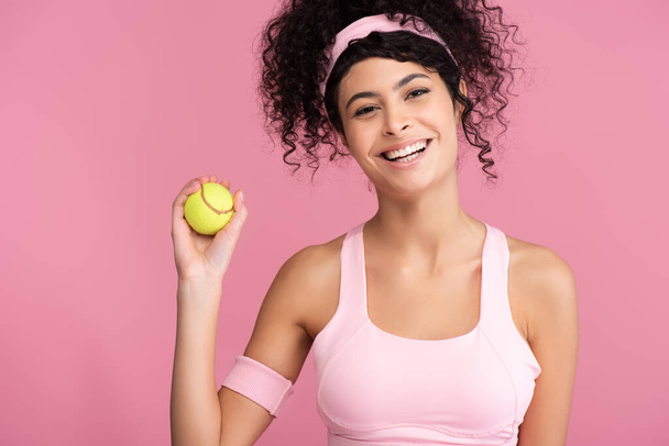 wesoła młoda kobieta trzyma piłkę tenisową odizolowany na różowy  - Zdjęcie, obraz