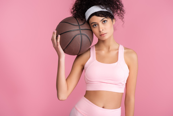 curly young woman holding basketball while looking at camera isolated on pink  - Φωτογραφία, εικόνα