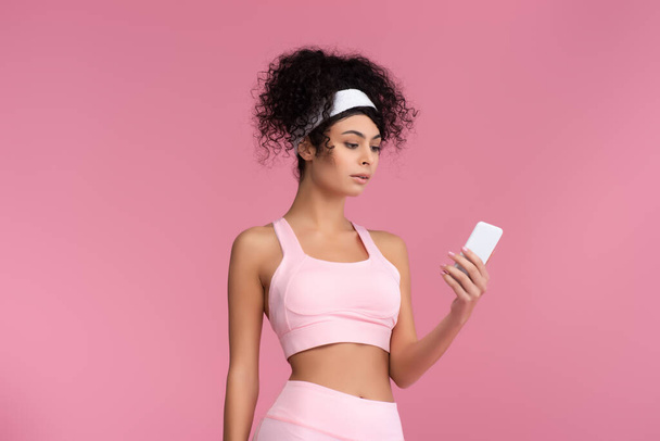 curly young sportswoman using smartphone isolated on pink  - Foto, Imagem