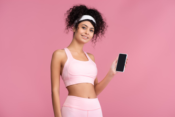 happy sportswoman holding smartphone with blank screen isolated on pink - 写真・画像