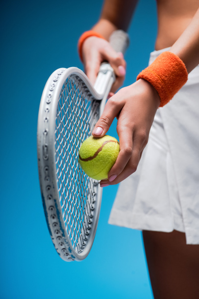 καλλιεργημένη άποψη του σπορ νεαρή γυναίκα κρατώντας ρακέτα τένις και μπάλα, ενώ παίζει σε μπλε - Φωτογραφία, εικόνα