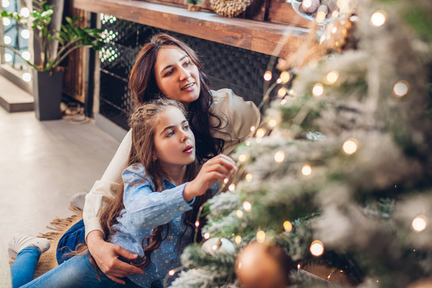 Mother and daughter admiring Christmas tree at home. Merry Christmas and Happy New Year. Family having fun enjoying winter holiday celebration - Photo, Image