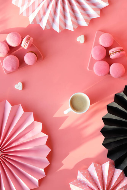 Creative monochrome flat lay on pink color paper. Happy Valentine Yummy macaroons and coffee. Folded paper fans and sugar hearts. Natural sunlight, long shadows. - Фото, изображение