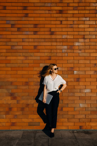 hermosa mujer joven con portátil en la calle frente a la pared de ladrillo rojo - Foto, Imagen