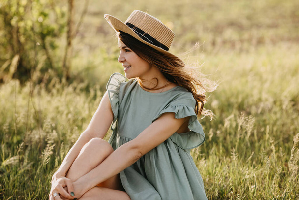 hermosa mujer joven en vestido y sombrero de paja en el jardín de manzana en la puesta del sol - Foto, imagen