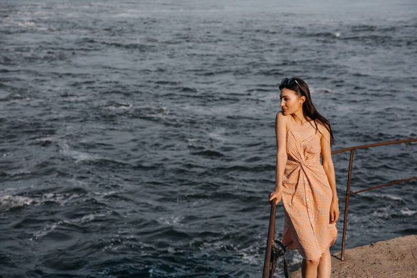 beautiful young woman in dress in front of beautiful seascape on sunny summer evening - Photo, Image