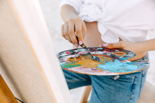 обрізаний знімок вагітної жінки-живописця, що малює абстрактну картину на відкритому повітрі в пісочниці
 - Фото, зображення