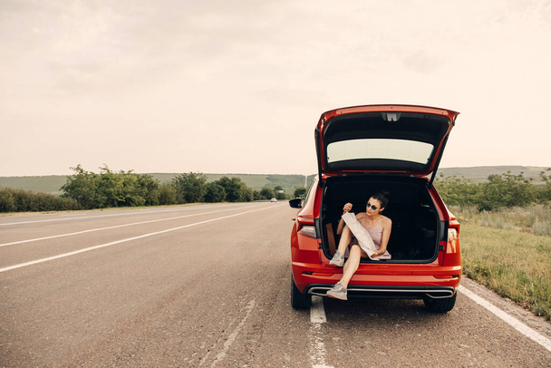 jovem mulher sentada no porta-malas do carro com mapa, tendo viagem de carro durante as férias de verão - Foto, Imagem