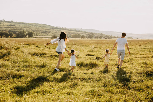 красивая молодая семья с двумя дочерьми, проводящая время вместе на природе - Фото, изображение