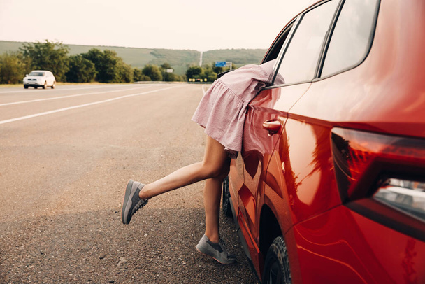 Kadının bacakları arabanın camından sarkıyor, yaz tatilinde araba yolculuğu yapıyor. - Fotoğraf, Görsel