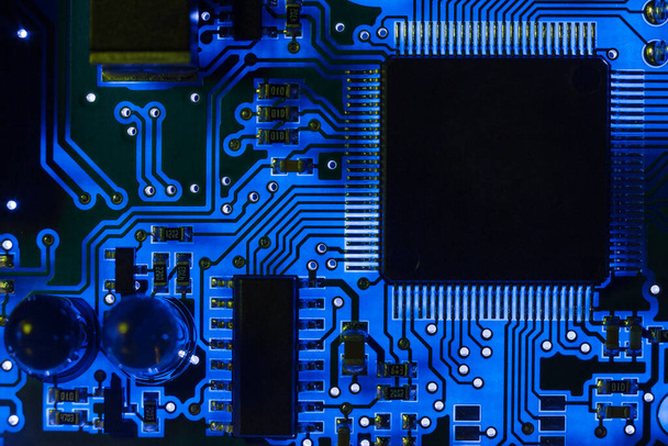 Close-up of a modern blue printed circuit board (PCB) with stripes of conductors between a transistor and an electronic equipment processor. IT technology repair in programming, upgrade and abstract macro background - Zdjęcie, obraz