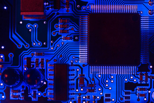 Close-up of a modern blue printed circuit board (PCB) with stripes of conductors between a transistor and an electronic equipment processor. IT technology repair in programming, upgrade and abstract macro background - Fotó, kép