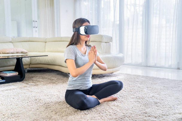 Młoda kobieta ćwiczy jogę i medytuje z okularami wirtualnej rzeczywistości w salonie w domu - Zdjęcie, obraz