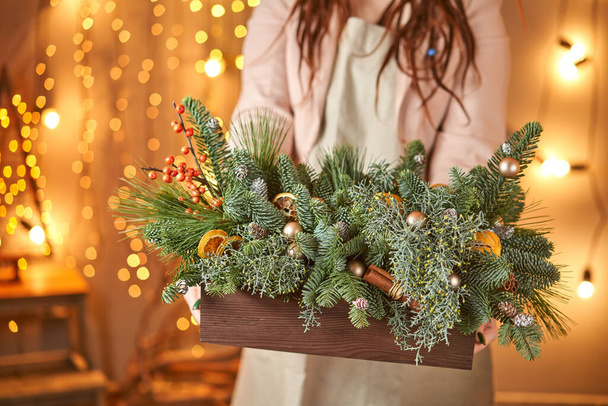 Giovane donna che tiene una scatola di legno di Natale con rami di abete per la vacanza. La celebrazione del nuovo anno. Negozio europeo di fiori - Foto, immagini