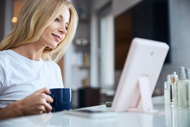 Щаслива весела блондинка жінка відпочиває в домашньому офісі за чашкою чаю або кави
 - Фото, зображення