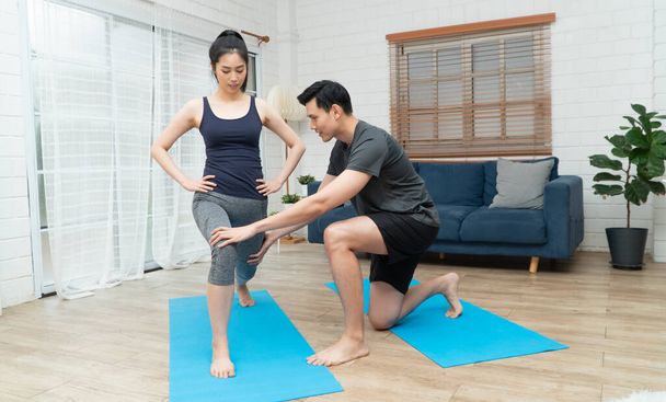 Terve nuori aasialainen pari harjoittelee kotona ja aviomies opettaa hänelle vaimon liikuntaa COVID-19 karanteenissa kotona. Uusi normaali elämäntapa ja terveellinen liikunta voidaan tehdä missä tahansa.. - Valokuva, kuva