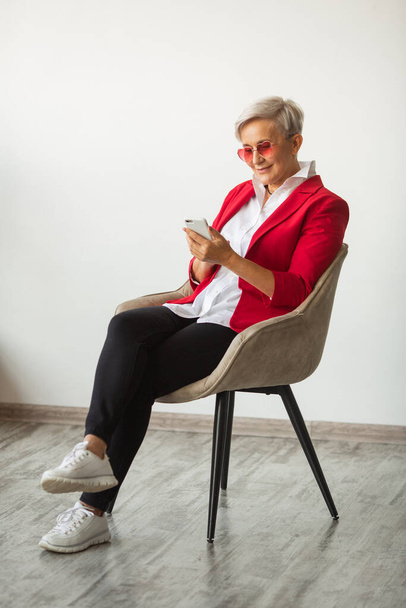 beautiful stylish woman aged in a red jacket with a mobile phone - Φωτογραφία, εικόνα