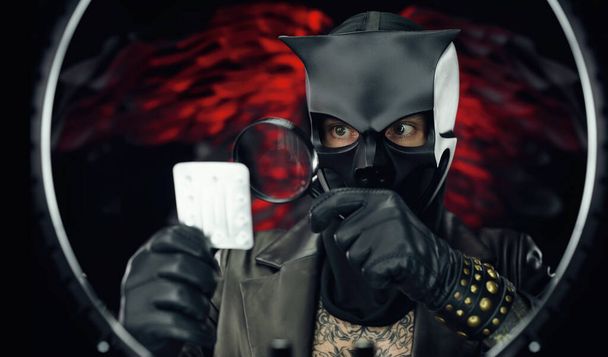 un hombre con una máscara de cráneo de demonio en una capa de cuero con una lupa y pastillas - doctor malvado - Foto, Imagen
