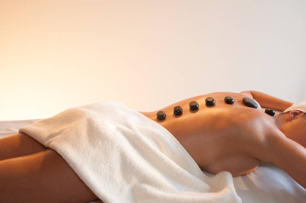Jeune femme caucasienne avec des pierres de lave chaudes sur le dos sur une table de massage dans un salon de beauté. Thérapie au spa. espace de copie - Photo, image