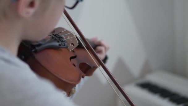  een jongen met een bril speelt viool, richt zich op de boog en muziekinstrument, de jongen is wazig. - Video