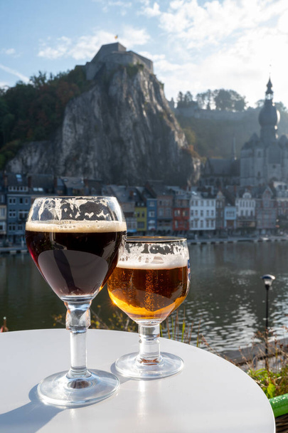 Drinking of dark and strong Belgian abbey beer with cheeses in sunny day with nice view on Maas river and town Dinant, Belgium - Photo, Image
