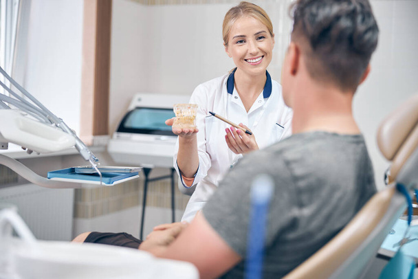 Веселая женщина-врач показывает модель челюсти пациенту - Фото, изображение