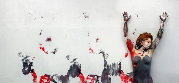 Joven mujer pelirroja pintada artísticamente abstracta con negro rojo blanco, pintura, desenrollándose en la pared del estudio, dejando impresiones artísticamente coloreadas de su hermoso cuerpo, espacio para copiar. - Foto, imagen