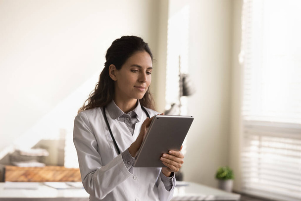 Женщина-врач работает на современном планшете в клинике - Фото, изображение