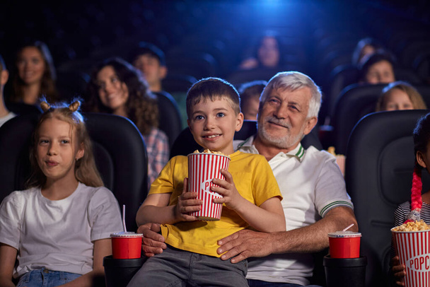 Grandfather with grandson on knees in cinema. - Foto, afbeelding