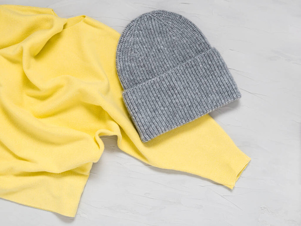 Bonnet et pull en maille gris aux couleurs tendance de l'année 2021 illuminant le jaune et le gris ultime. Vêtements et accessoires d'automne et d'hiver chauds à la mode. Texture de laine sur fond de béton - Photo, image