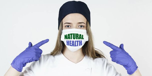 Medicine concept. The doctor points his fingers at the mask with the inscription - NATURAL HEALTH - Foto, Bild