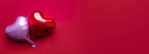 on a red background there are two heart-shaped foil balloons - red and purple - Фото, зображення